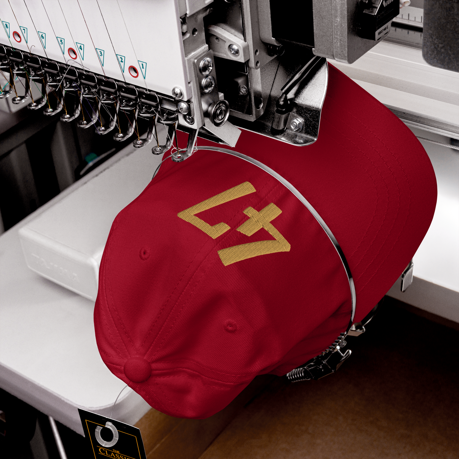 Cranberry cap with gold logo being embroidered on a machine.